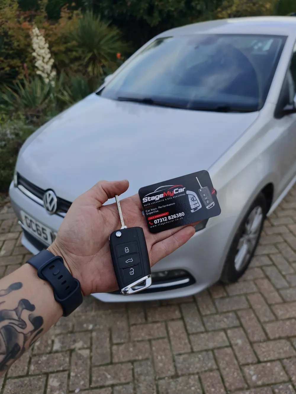 Replacement VW flip key and StageMyCar business card in front of a silver VW Polo