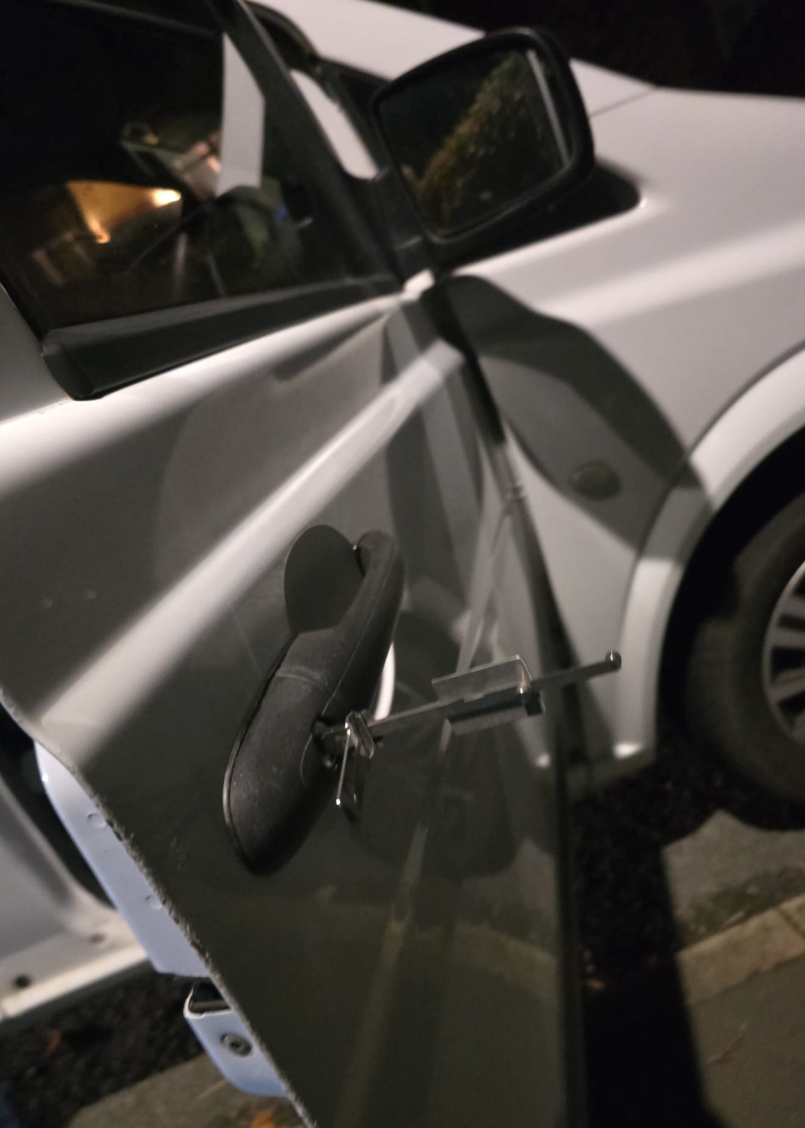 Mobile auto locksmith performing non-destructive car unlock at night on a silver vehicle